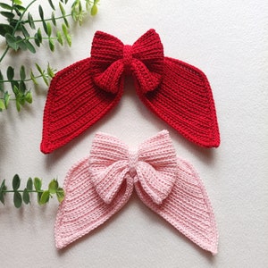 May include: Two crocheted hair bows, one red and one pink, with a large bow in the centre and two long tails.