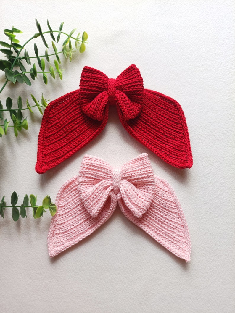 May include: Two crocheted hair bows, one red and one pink, with a large bow in the centre and two long tails.