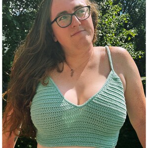Puede incluir: Una mujer con un top corto de crochet verde claro con escote en V. Lleva pantalones negros y tiene el pelo largo y casta&ntilde;o.