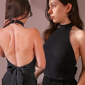 May include: A black halter top with a high neckline and open back, tied with a bow. The top is made of a crocheted material. The model is wearing black pants.
