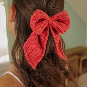 Può includere: Un fermaglio per capelli a forma di fiocco in crochet color corallo. Il fiocco è legato in un grande nodo morbido e ha code lunghe e fluide.