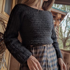 May include: A dark gray, long-sleeved sweater with a boat neck. The sweater has a textured knit pattern and is paired with a plaid skirt. The outfit is suitable for fall or winter wear.