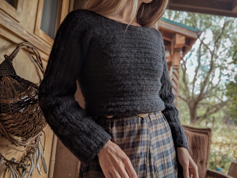 May include: A dark gray, long-sleeved sweater with a boat neck. The sweater has a textured knit pattern and is paired with a plaid skirt. The outfit is suitable for fall or winter wear.