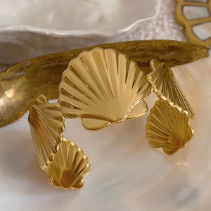 May include: A gold-toned bracelet with a design of three overlapping seashells.