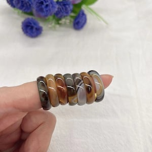 Puede incluir: Una pila de ocho anillos de ágata en tonos marrones, grises y blancos. Los anillos están apilados en un dedo.