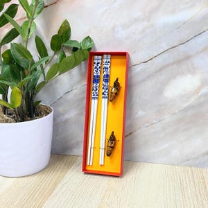 May include: A set of two white chopsticks with blue and white floral designs, in a red box with two butterfly-shaped chopstick rests.