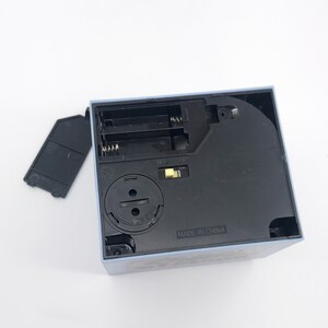 May include: A light blue square box with a black base, showing the battery compartment and an on/off switch. The battery cover is detached. The text "MADE IN CHINA" is visible on the base.