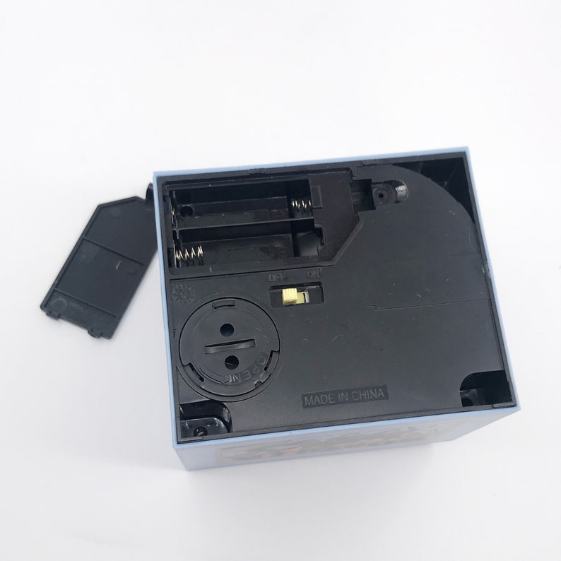 May include: A light blue square box with a black base, showing the battery compartment and an on/off switch. The battery cover is detached. The text "MADE IN CHINA" is visible on the base.