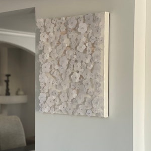May include: White canvas wall art featuring a 3D design of white paper flowers. The flowers are arranged in a dense pattern, creating a textured and organic look.