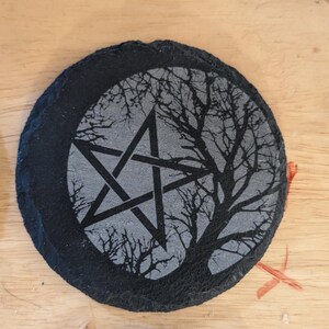Pode incluir: Um descanso de copo de ardósia preto com um pentagrama cinza e uma silhueta de uma árvore com galhos nus.