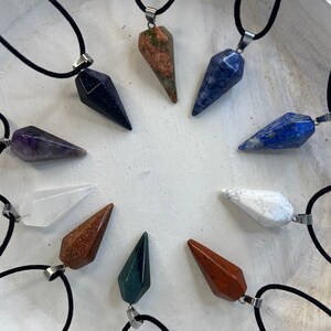 May include: Ten crystal point pendants on black cords. The points are made of various stones, including amethyst, clear quartz, lapis lazuli, red jasper, and green aventurine.