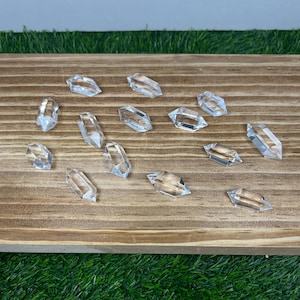 May include: Clear crystal quartz points arranged on a wooden surface. The crystals are faceted and reflect light, showcasing their clarity and shape. The crystals are a light, transparent color.