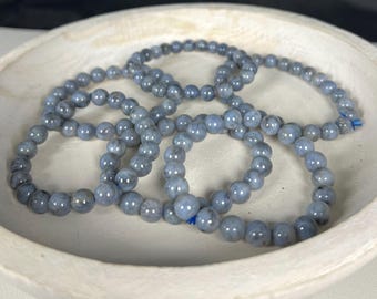 May include: A set of six gray gemstone bracelets with a smooth, polished finish. The bracelets are made of round beads and are stacked on top of each other.