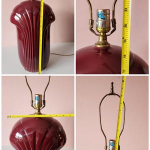 May include: A burgundy ceramic table lamp with a brass neck and a shade that is approximately 22 inches tall. The lamp has a fluted design and a classic, vintage aesthetic. The lamp is shown from multiple angles.