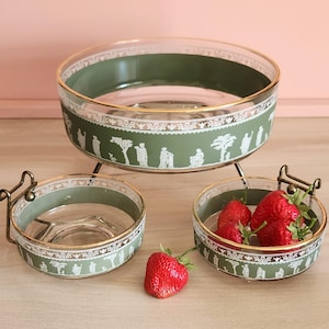 May include: A three-tiered serving set with a green and white design. The set includes a large bowl and two smaller bowls, all with a gold rim. The bowls are filled with strawberries. The set is supported by a gold metal stand.