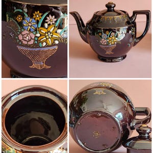 May include: A dark brown ceramic teapot with a lid, featuring a floral design in a basket. The teapot has a spout and handle, with gold accents along the rim and base. The floral design includes pink, yellow, blue, and white flowers.