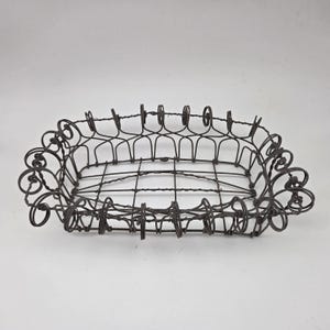 May include: A rectangular wire basket constructed from dark brown metal. The base features a grid pattern, while the upper rim is decorated with a series of repeated circular wire loops that extend around the entire perimeter of the basket.