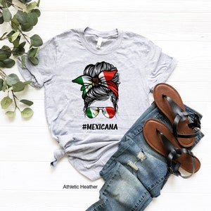 May include: Gray t-shirt with a graphic of a woman's hair in a bun with a bandana featuring the Mexican flag. The text "#MEXICANA" is printed below the graphic.