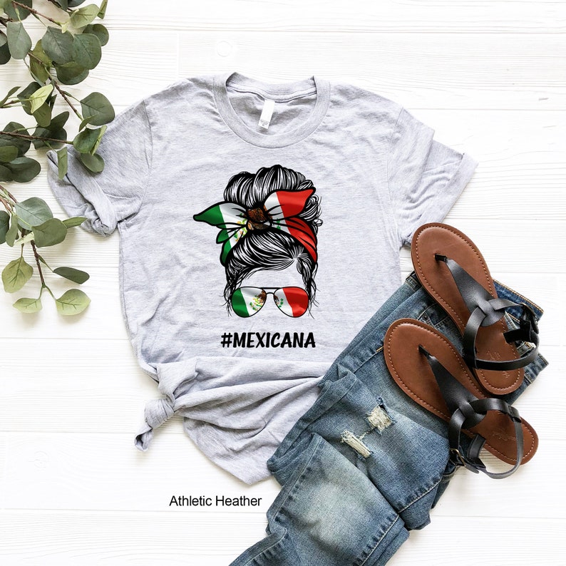 May include: Gray t-shirt with a graphic of a woman's hair in a bun with a bandana featuring the Mexican flag. The text "#MEXICANA" is printed below the graphic.