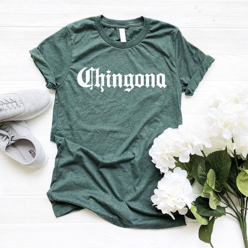 May include: A dark green t-shirt with the word "Chingona" printed in white on the front. The shirt is made of a soft, comfortable material and has a relaxed fit.