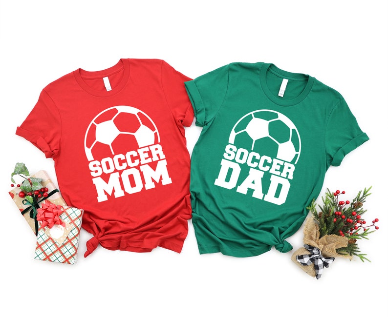 May include: Two t-shirts, one red and one green, with a white soccer ball graphic and the text "Soccer Mom" and "Soccer Dad" in white.
