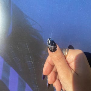 Op de afbeelding: Een hand met lange, donkerblauwe vingernagels. E&eacute;n nagel heeft de tekst "HARD & SOFT" met sterontwerpen op een zwarte achtergrond. Andere nagels hebben een dambordpatroon en een blauw-wit ontwerp.