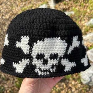 Puede incluir: Gorro de punto negro con un diseño de calavera y huesos cruzados blancos.