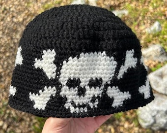 Puede incluir: Gorro de punto negro con un diseño de calavera y huesos cruzados blancos.