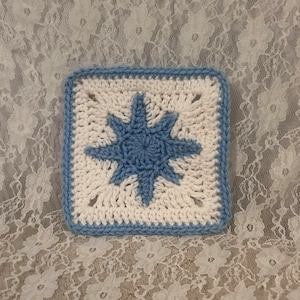 May include: A blue and white crocheted square with a star design in the center.