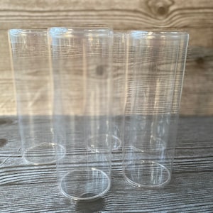 Op de afbeelding: Vier heldere, cilindrische drinkglazen. De glazen zijn gemaakt van transparant materiaal, waardoor een volledig zicht op de binnenkant mogelijk is. De glazen zijn in een groep gerangschikt en tonen hun eenvoudige, maar elegante ontwerp. De glazen zijn leeg en klaar om te worden gevuld.