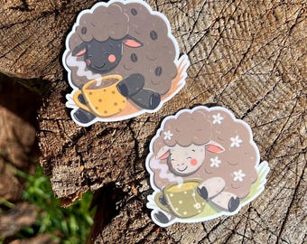 May include: Two stickers featuring sheep illustrations. One sheep is brown with coffee bean accents, holding a yellow polka-dot mug. The other sheep is light brown with flower accents, holding a green floral mug. Both are smiling.