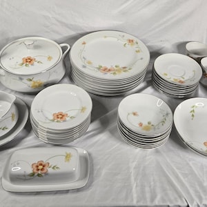 May include: A white porcelain dinnerware set featuring a delicate floral pattern with orange and yellow flowers and green stems. The collection includes a coffee pot, lidded tureen, butter dish, gravy boat, creamer, sugar bowl, plates, bowls, and cups.