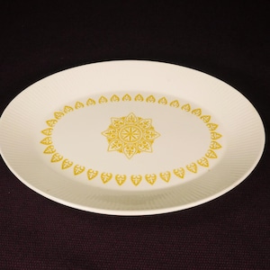 May include: Oval serving platter with a cream-colored base and a gold floral design. The platter has a textured rim and a central medallion design, suitable for serving appetizers or entrees.