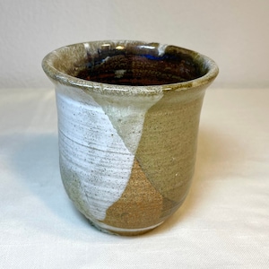 Peut inclure: Un vase en céramique blanc, brun et beige avec un glaçage moucheté. Le vase a un fond arrondi et une large ouverture.