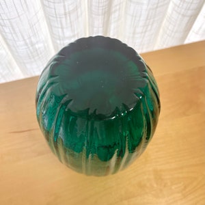 May include: A dark green glass vase with a ribbed design. The vase is round and has a wide opening.