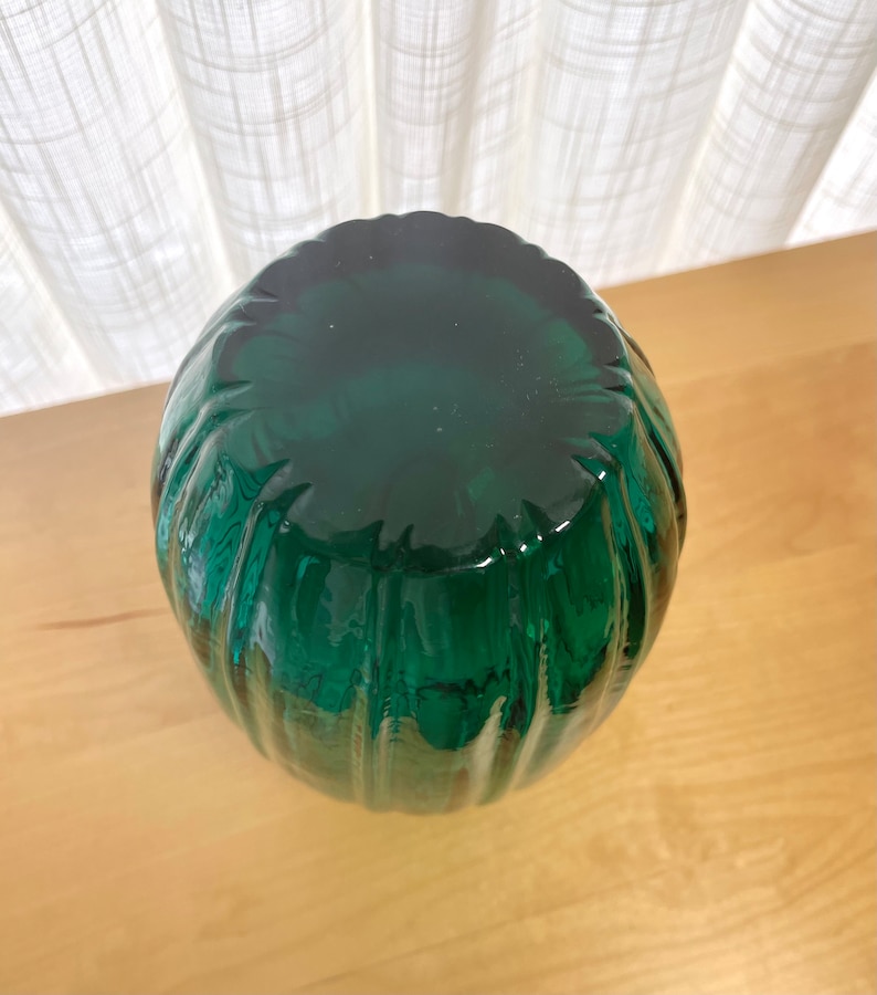 May include: A dark green glass vase with a ribbed design. The vase is round and has a wide opening.