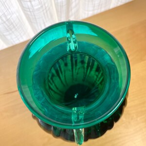 May include: A green glass vase with a textured surface and three handles. The vase is empty and has a wide opening.