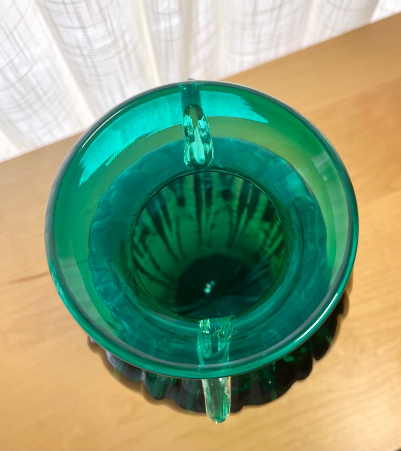 May include: A green glass vase with a textured surface and three handles. The vase is empty and has a wide opening.