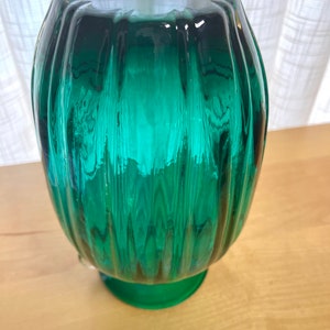 May include: A teal green glass vase with a ribbed design and a round base.