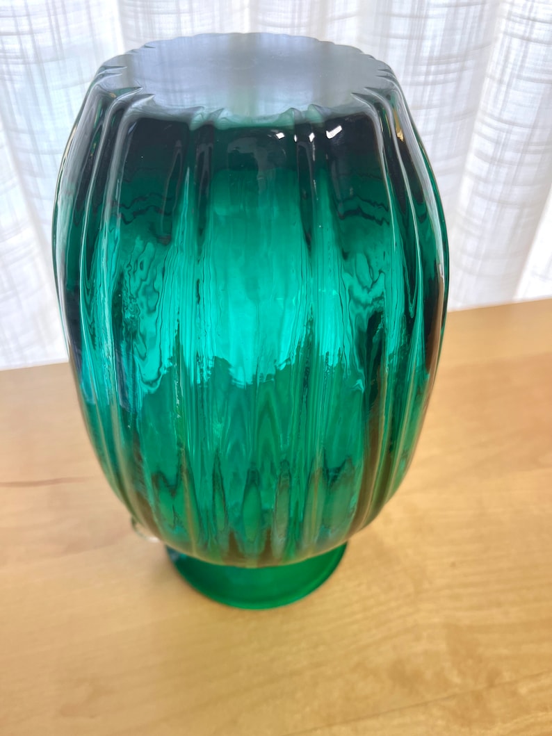 May include: A teal green glass vase with a ribbed design and a round base.