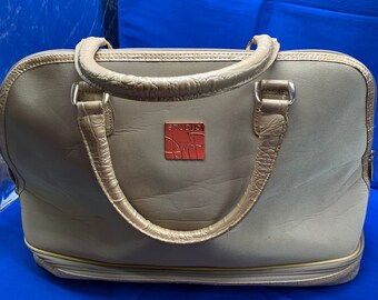 May include: A beige canvas handbag with gold-colored accents and a zipper closure. The bag has two top handles and a logo patch that reads "Studio 1 Art".