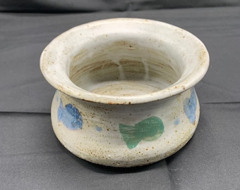 May include: A white ceramic bowl with a wide rim and a rounded base. The bowl is decorated with blue and green abstract shapes.