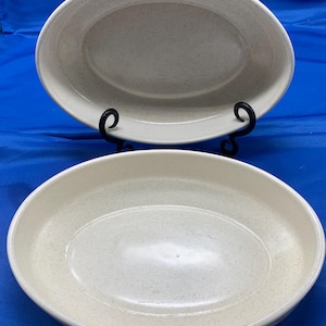 May include: Two white oval ceramic baking dishes with a speckled finish. The dishes are empty and have a slight lip around the edge.