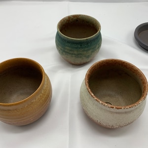 May include: Three ceramic pots in different colors and patterns. The pots are all round and have a wide opening. The pots are perfect for planting small plants or succulents.