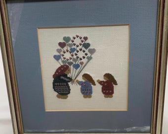A hand cross-stitch, lady selling heart shaped balloons.