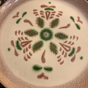 May include: A white ceramic plate with a brown and green floral design. The plate has a speckled brown rim.