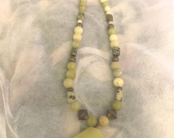 May include: A green jade stone necklace with a large, faceted pendant. The necklace is made of various shades of green and white beads with bronze accents.
