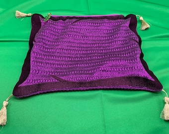 May include: A purple velvet pillow with a decorative border and tassels. The pillow has a quilted texture and a subtle sheen.