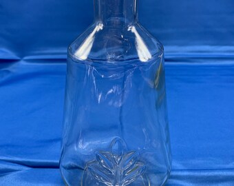 May include: A clear glass bottle with a wide mouth and a textured leaf design at the bottom.
