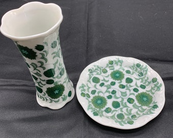 Puede incluir: Un jarrón de porcelana blanca y un plato a juego con un patrón floral verde. El jarrón tiene un borde festoneado y el plato tiene un borde festoneado.